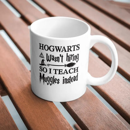 White mug with black text on a wooden surface Hogwarts Wasn’t Hiring, So I Teach Muggles Instead Mug