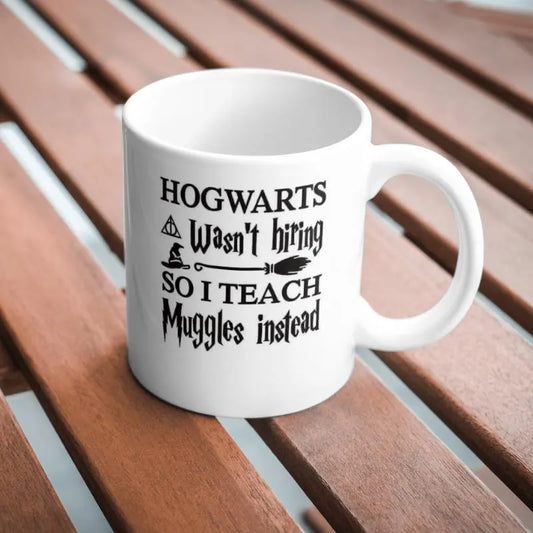 White mug with black text on a wooden surface Hogwarts Wasn’t Hiring, So I Teach Muggles Instead Mug