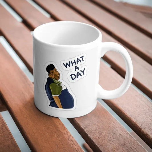What a Day” Mug – Relatable Sarcasm for Everyday Chaos. White mug with a graphic of a person and 'What a Day' text on a wooden surface