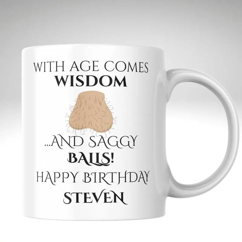 With Age Comes Wisdom… and Saggy Balls Birthday Mug. White mug with humorous birthday message and graphic on a light gray background